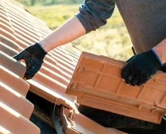 Mains gantées remplaçant une tuile en terre cuite